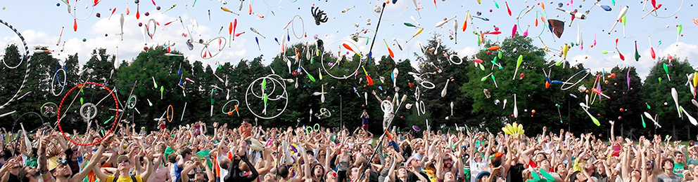 A crowd of people throwing juggling props into the air outside