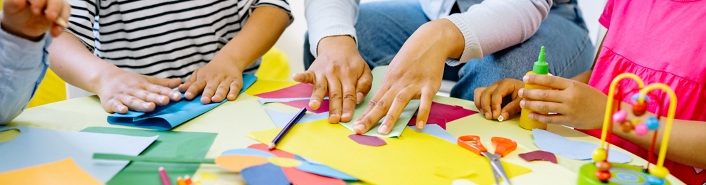 Closeup of teacher and students' hands working with construction paper on a table