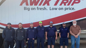 Six Kwik Trip employees completing the commercial driver's license for truck driving stand in front of a trailer that reads Kwik Trip, with their instructor, Val Gunmundson standing alongside them at the far right.