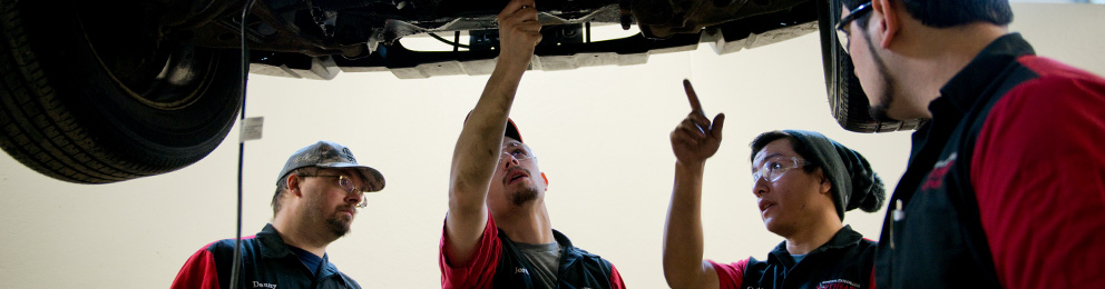 Three mechanics working under a car on a lift
