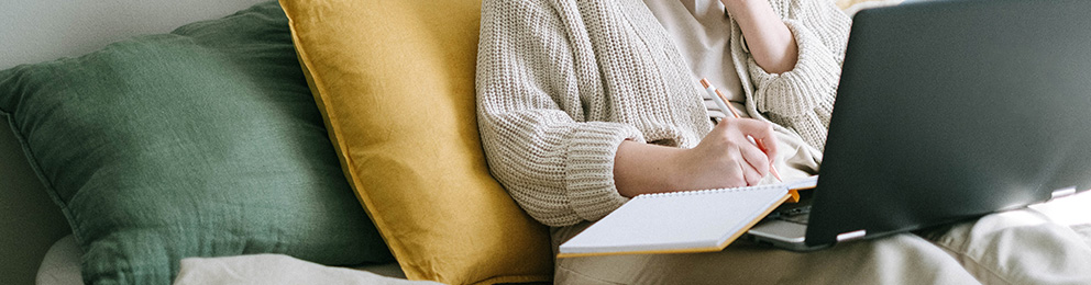 person sitting on couch with pillow behind them and laptop open on lap
