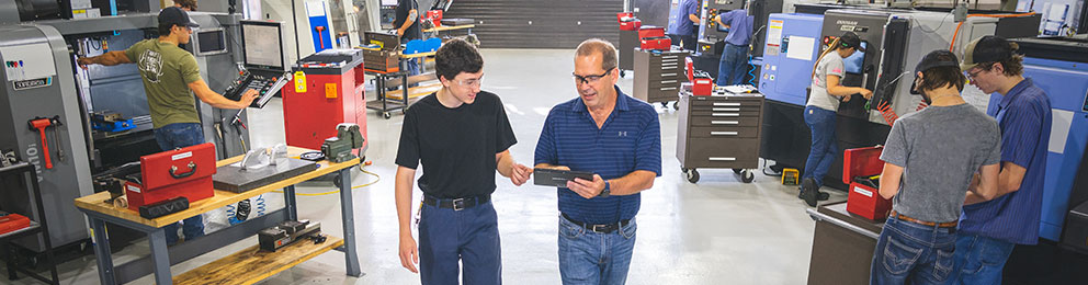 Instructor talking with student walking in machine shop