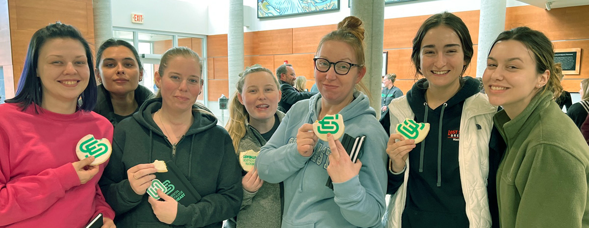 Group of students seen in lobby of Winona campus holding cookies with SE logo on the front of the cookie