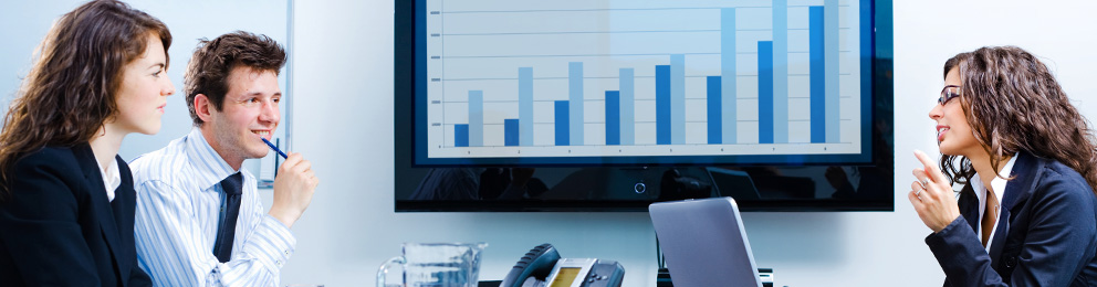 Three professionals working with a graphic of a bar chart on a wall monitor