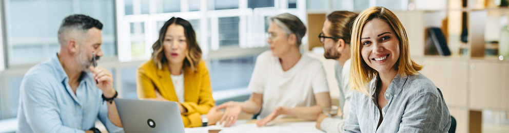 Woman smiling at a meeting table with other workers in the background